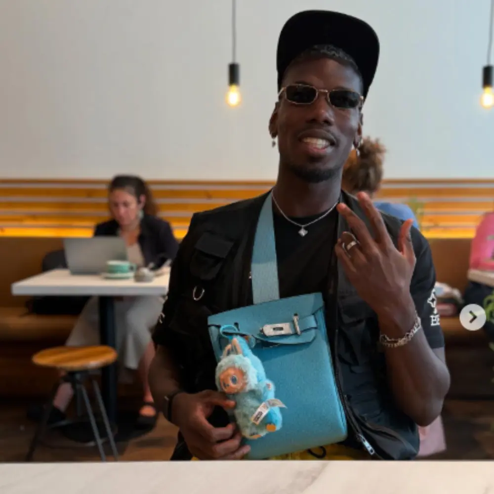 Paul Pogba affichant un sac bleu décoré de mini peluches POP MART suspendues